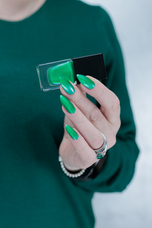 Female hand with long nails and bright green manicure with bottles of nail polishの写真素材