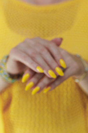 Female hand with long nails and a bottle of bright yellow orange nail polishの写真素材