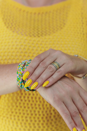 Female hand with long nails and a bottle of bright yellow orange nail polishの写真素材