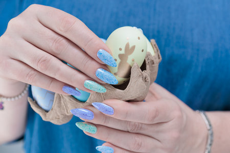 Women's hands with multi-colored manicure hold Easter eggs. Light yellow, blue and green color.の写真素材