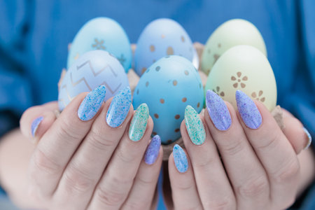 Women's hands with multi-colored manicure hold Easter eggs. Light yellow, blue and green color.