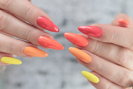 Multicolored manicure, female hands with colored nails, nail polishes, yellow, orange and pink...