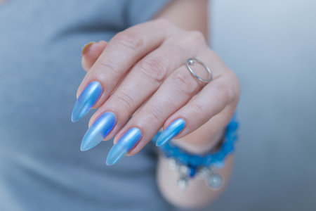Woman's beautiful hand with long nails and blue manicure with bottles of nail polishの写真素材