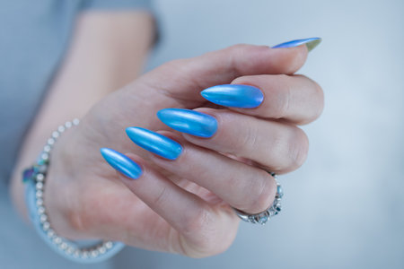Woman's beautiful hand with long nails and blue manicure with bottles of nail polishの写真素材