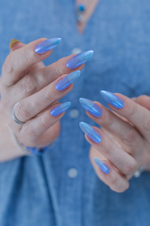 Woman's beautiful hand with long nails and blue manicure with bottles of nail polishの写真素材