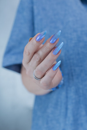 Woman's beautiful hand with long nails and blue manicure with bottles of nail polishの写真素材