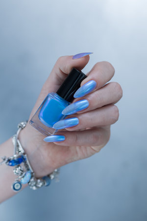 Woman's beautiful hand with long nails and blue manicure with bottles of nail polishの写真素材