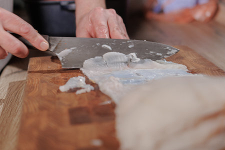 Male hands cutting white fish on a wooden board