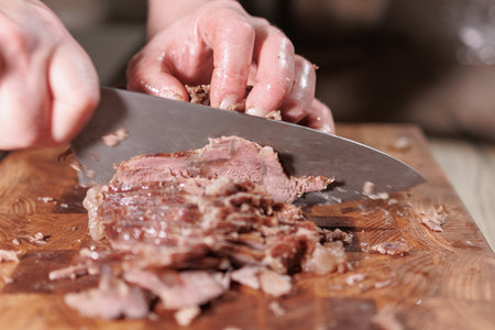 Male hands cutting cooked meat beef on a wooden boardの写真素材