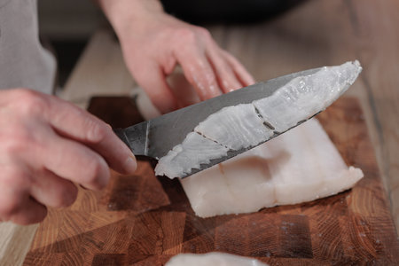 Male hands cutting white fish on a wooden boardの写真素材