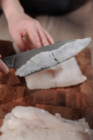 Male hands cutting white fish on a wooden boardの写真素材