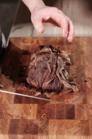 Male hands cutting cooked meat beef on a wooden boardの写真素材