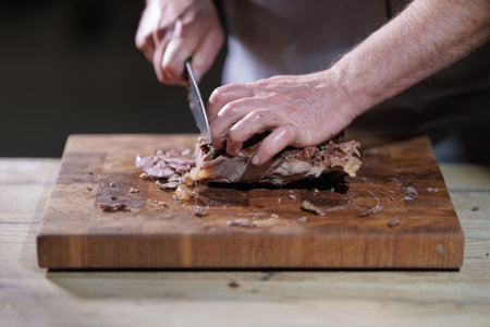 Male hands cutting cooked meat beef on a wooden boardの写真素材