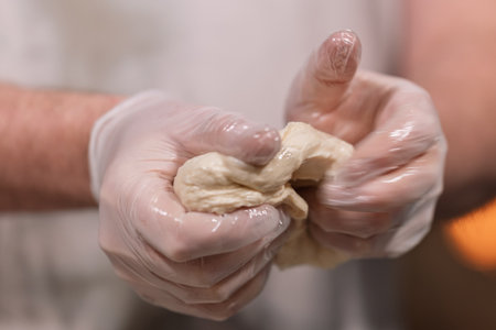 Hands in gloves kneading dough for bakingの写真素材