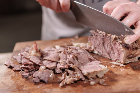 Male hands cutting cooked meat beef on a wooden boardの写真素材