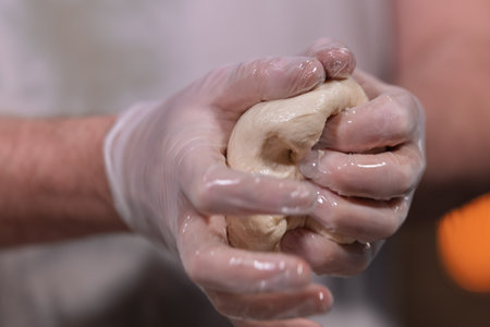 Hands in gloves kneading dough for bakingの写真素材