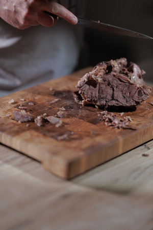 Male hands cutting cooked meat beef on a wooden boardの写真素材