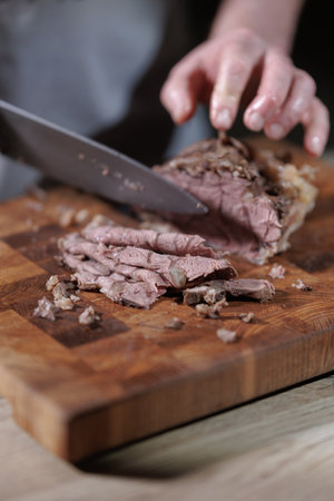 Male hands cutting cooked meat beef on a wooden boardの写真素材