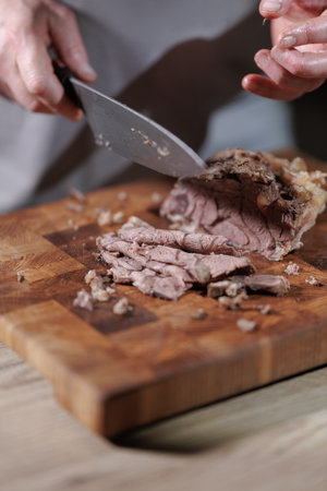 Male hands cutting cooked meat beef on a wooden boardの写真素材