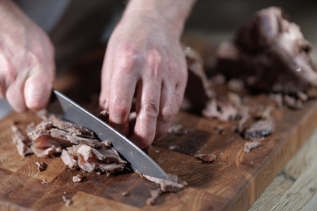 Male hands cutting cooked meat beef on a wooden board
