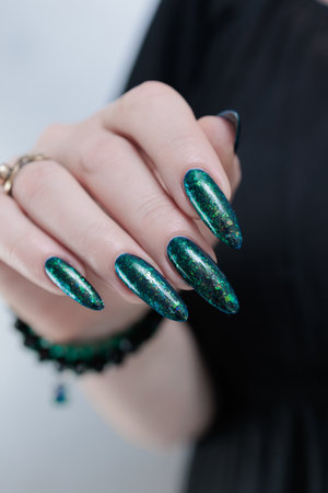 Woman's hand with long nails and black green nail polishの写真素材