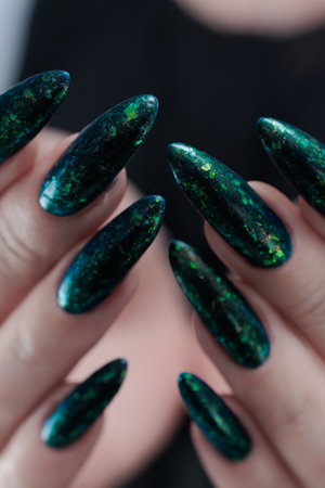 Woman's hand with long nails and black green nail polishの写真素材