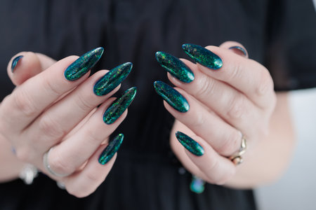 Woman's hand with long nails and green blue nail polishの写真素材
