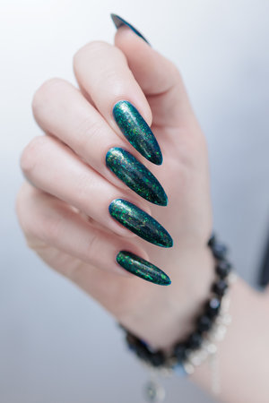 Woman's hand with long nails and black green nail polishの写真素材