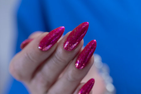 Female hand with long nails and a bottle bright neon pink fuchsia color nail polishの写真素材
