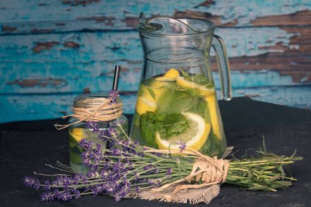 Jug and glass of fresh lemonade on blue wooden background