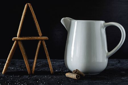 Jug of white milk accompanied by cinnamon cookies on dark backgroundの写真素材