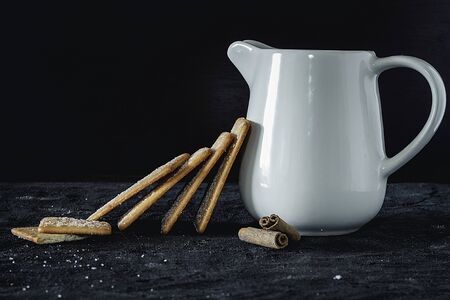 Jug of white milk accompanied by cinnamon cookies on dark backgroundの写真素材