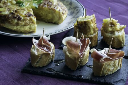 Skewers of serrano ham and potato omelette on slate dishesの写真素材