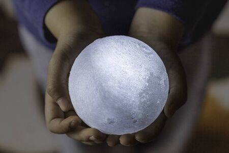 Child hands holding bright illuminated moon Conceptual hold on to your dreams, the unreachableの写真素材