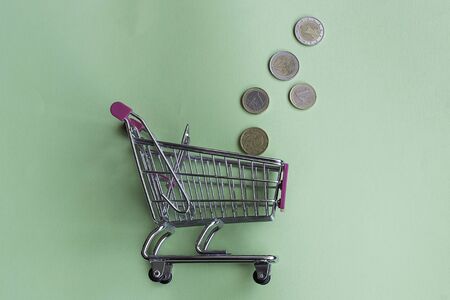Supermarket cart with coins on green background. Concept of home economicsの写真素材