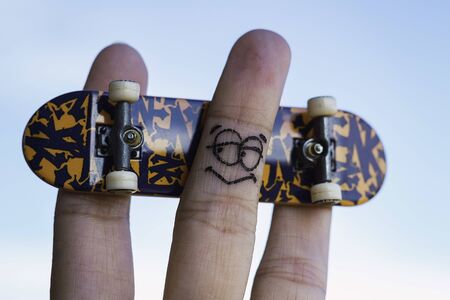 Fingers with a painted face playing with a small skateboard Fingers posing with a toy skateboardの写真素材