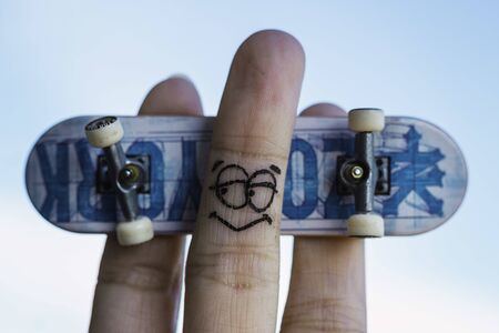 Fingers with a painted face playing with a small skateboard Fingers posing with a toy skateboardの写真素材