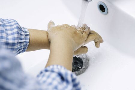 Child hands in school coat washing their hands under the tapの写真素材