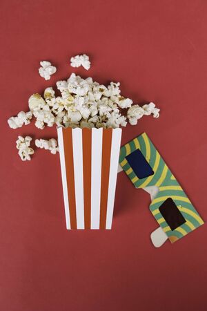 Popcorn in cardboard box on red background Conceptual cinema, watch a movieの写真素材