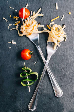 Pair of forks with rolled spaghetti, cherry tomatoes and zucchini Conceptual of healthy food, new trend veganismの写真素材