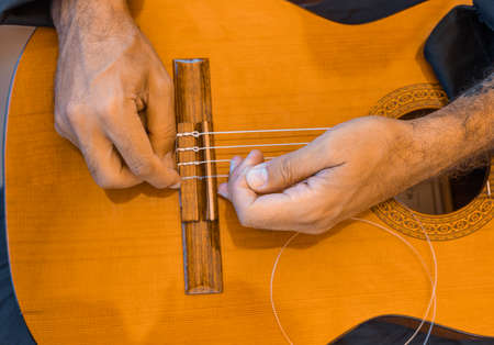 Male hands changing the strings of a classical guitar Luthier putting nylon strings on a Spanish...