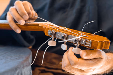 Male hands changing the strings of a classical guitar Luthier putting nylon strings on a Spanish...