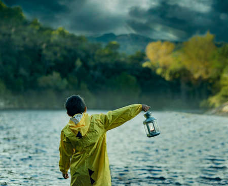Boy on his back in a lake with a yellow raincoat and a lantern in one handの写真素材