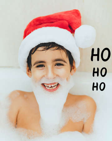Smiling boy in the bathtub with Santa's hat and a foam beardの写真素材