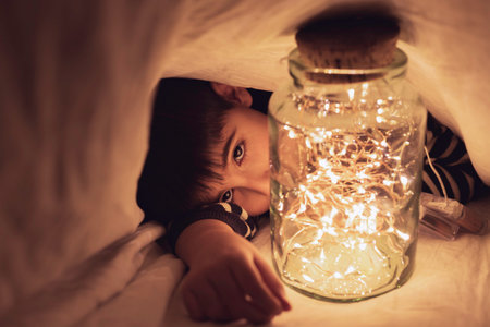 Child plays under the sheet with a pot of warm lights