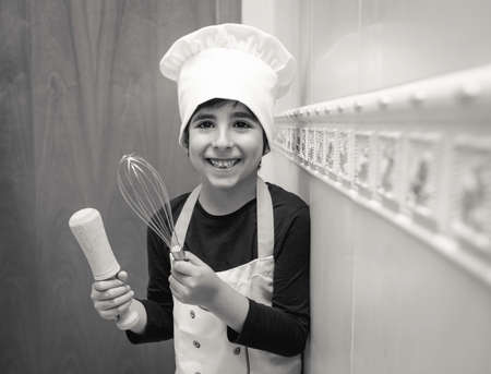 Smiling boy poses in the kitchen of his house with chef uniformの写真素材
