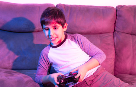 Boy plays video games from the couch under red and blue lightsの写真素材