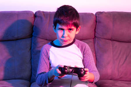 Boy plays video games from the couch under red and blue lightsの写真素材