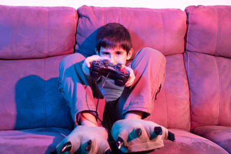 Boy plays video games from the couch under red and blue lights