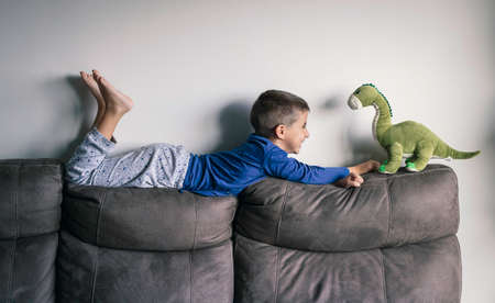 Smiling child plays on the sofa at home with a stuffed dinosaurの写真素材
